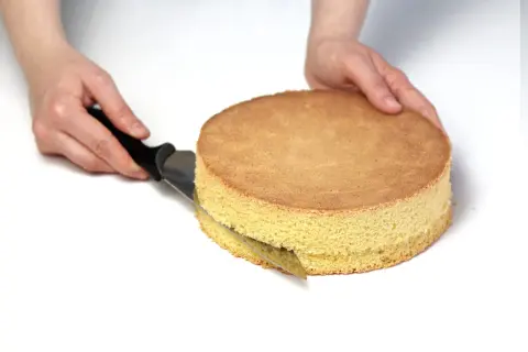 Ręce kroją biszkopt nożem, przygotowując go do dalszych etapów przepisu na tort.