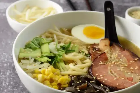 Pyszny ramen przepis: miska pełna makaronu, jajko na twardo, plastry boczku, warzywa i kiełki. Idealny na chłodne dni.
