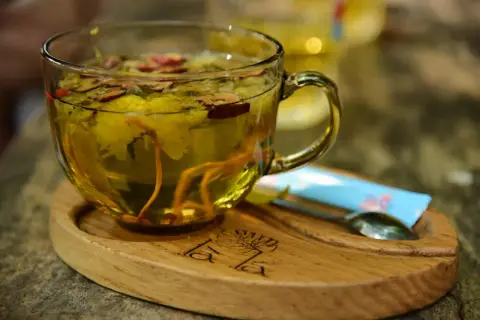Aromatyczna herbata z dodatkiem imbiru do herbaty, kwiatów i jagód. Podana w szklanej filiżance na drewnianej podstawce.
