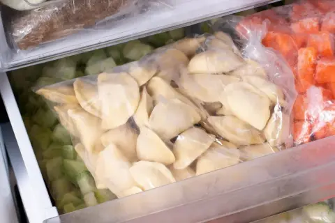 W zamrażarce leżą torby z mrożonkami: pierogi, zielone warzywa i marchewka.