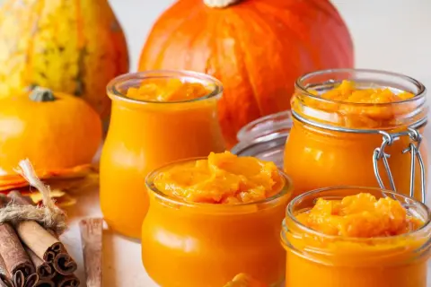Słoiczki z domowym puree z dyni, obok świeżych dyni i przypraw. Idealne na jesienne wypieki.