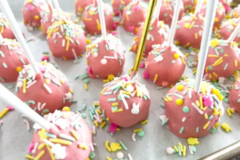 Różowe cake pops z kolorową posypką i króliczkami, idealne na wielkanocny przepis.