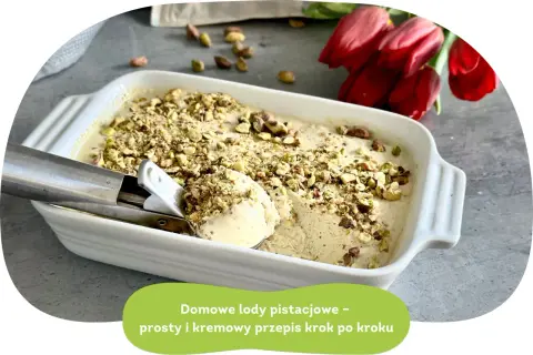 Domowe lody pistacjowe w białej misce, posypane orzechami. Obok czerwone tulipany i gałka lodów na łyżce.