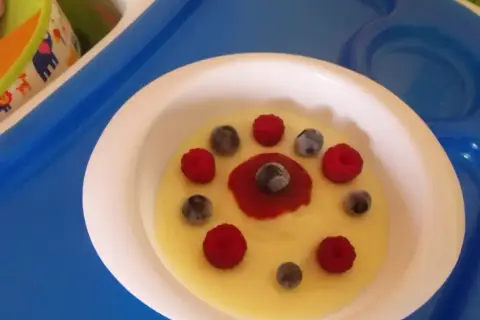 Pyszna kasza manna na wodzie, udekorowana malinami i borówkami, wygląda jak słoneczko na talerzu.