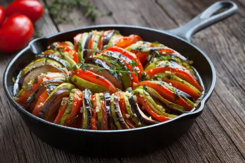 Ratatouille w żeliwnej patelni, klasyka kuchni francuskiej. Warzywa ułożone wachlarzowo, skropione ziołami.