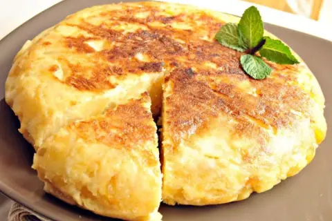 Pyszna tortilla de patatas, złocista i puszysta, z gałązką mięty na wierzchu.