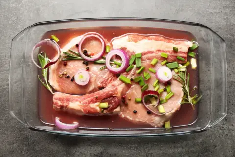 Peklowanie mięsa do pieczenia w szklanym naczyniu z cebulą, rozmarynem i pieprzem.