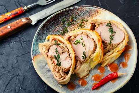 Pyszne ciasto francuskie na obiad, z soczystym mięsem i farszem, ozdobione gałązkami tymianku i papryczką chili.