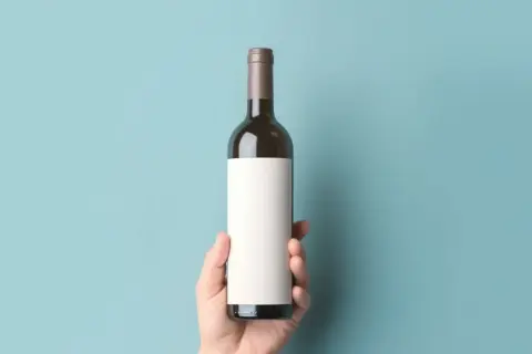 Dłoń trzyma butelkę z pustą etykietą, idealną na wino bezalkoholowe.