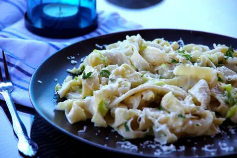 Pyszny makaron z porem, posypany parmezanem i świeżą natką pietruszki, czeka na widelcu.