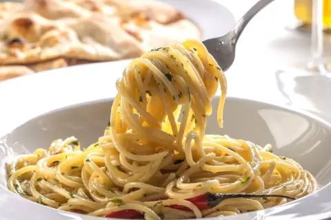 Pyszny, aromatyczny makaron spaghetti z czosnkiem i chili, idealny przepis na szybki makaron. Na talerzu widać też pieczywo.