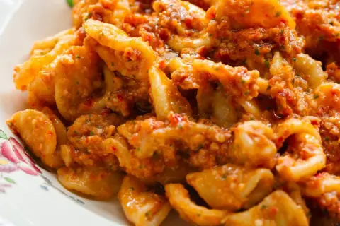 Pyszny makaron z pesto, pełen aromatycznych ziół i pomidorów, podany na talerzu z delikatnym wzorem.