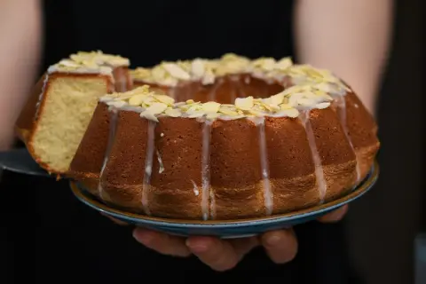 Wilgotna babka wielkanocna, ozdobiona lukrem i płatkami migdałów, prezentuje się apetycznie. Kawałek ciasta został już odcięty.