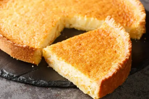 Złociste ciasto z wyciętym kawałkiem, idealne na listę 10 najlepszych ciast. Puszyste wnętrze i chrupiąca skórka.