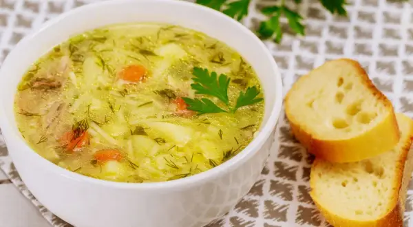 Aromaticzna zupa wiosenna z kawałkami kurczaka, ziemniaków i marchewki, posypana świeżym koperkiem. Obok kromki chleba.