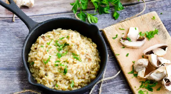 Kremowe risotto z grzybami, posypane natką pietruszki. Idealny przepis na pyszny obiad.