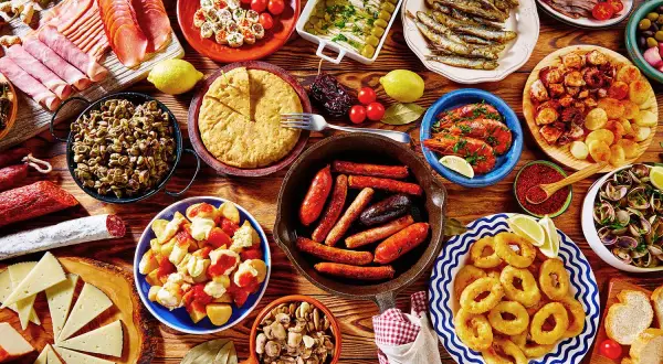 Tapas co to? Kolorowy stół pełen hiszpańskich przekąsek: kiełbaski, krewetki, kalmary, owoce morza, ser, tortilla i wędliny.