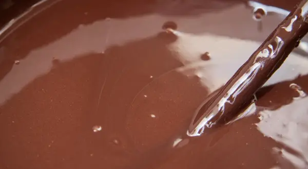 Gładki, błyszczący ganache czekoladowy w misce, z widoczną drewnianą łyżką zanurzoną w jego aksamitnej masie.