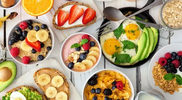 Kolorowe śniadanie dla dzieci: owsianka z owocami, tosty z awokado i jajkiem, płatki z jagodami, smoothie, jajka sadzone z awokado i sok pomarańczowy.