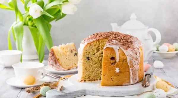 Pyszna babka panettone z lukrem i czekoladą, ozdobiona wielkanocnymi pisankami i białymi tulipanami.