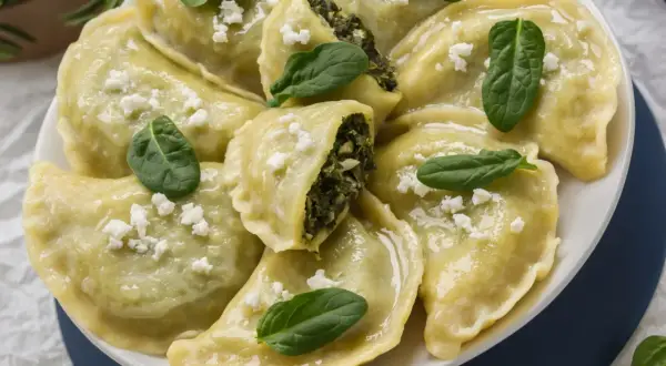 Pyszne pierogi ze szpinakiem i fetą, posypane świeżymi listkami i białym serem. Idealne z czymś lekkim!