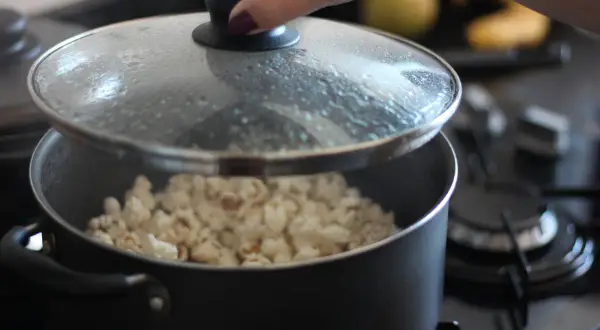 Ręka podnosi pokrywkę garnka, odsłaniając pyszny, świeżo zrobiony popcorn. Idealny sposób, jak zrobić popcorn na wieczór filmowy.