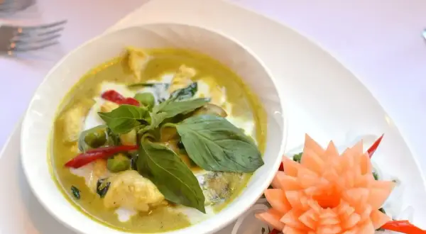 Zielony curry z kurczakiem, podany z bazylią i papryczką chili. Obok ozdobna rzeźba z marchewki.