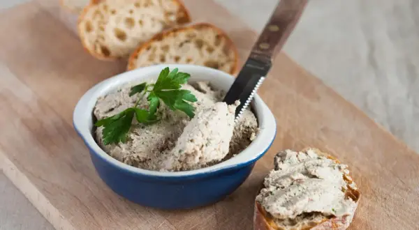 Pyszna pasta z gotowanego kurczaka na chrupiącym pieczywie, udekorowana natką pietruszki. Idealna na przekąskę.