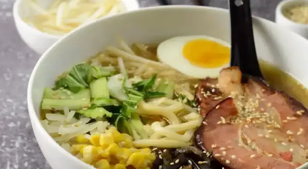 Pyszny ramen przepis: miska pełna makaronu, jajko na twardo, plastry boczku, warzywa i kiełki. Idealny na chłodne dni.