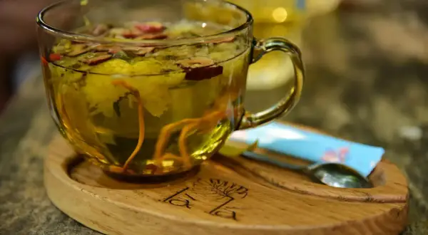 Aromatyczna herbata z dodatkiem imbiru do herbaty, kwiatów i jagód. Podana w szklanej filiżance na drewnianej podstawce.