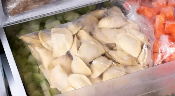 W zamrażarce leżą torby z mrożonkami: pierogi, zielone warzywa i marchewka.