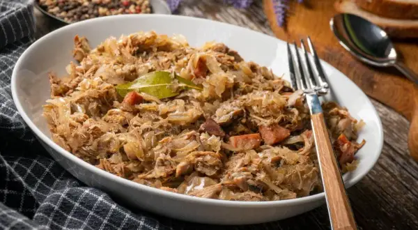 Pyszny bigos w białej misce, z widelcem. Zastanawiasz się, ile może stać bigos w lodówce? Nawet kilka dni, a smakuje coraz lepiej!