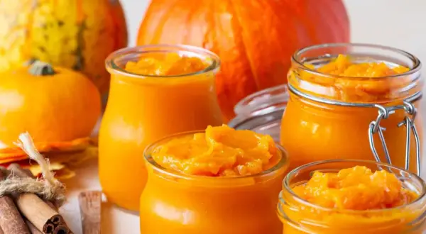 Słoiczki z domowym puree z dyni, obok świeżych dyni i przypraw. Idealne na jesienne wypieki.