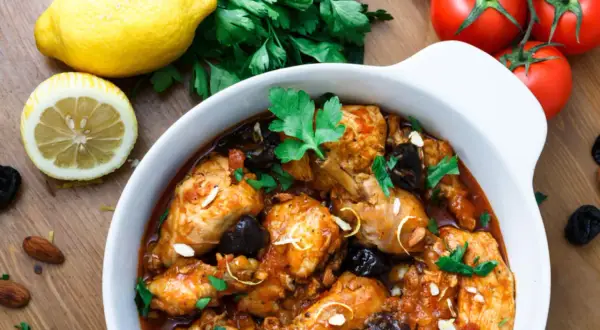 Aromatyczny tagine z kurczakiem, śliwkami i migdałami, podany z cytryną i pomidorami.
