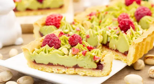 Pyszny mazurek pistacjowy z malinami i chrupiącymi pistacjami, udekorowany zielonym kremem.