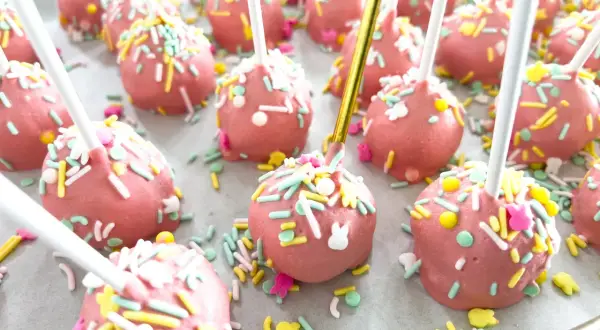 Różowe cake pops z kolorową posypką i króliczkami, idealne na wielkanocny przepis.