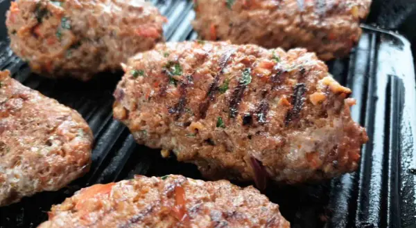 Kebab Adana grillowany na patelni grillowej, z widocznymi kawałkami pomidorów i ziół.