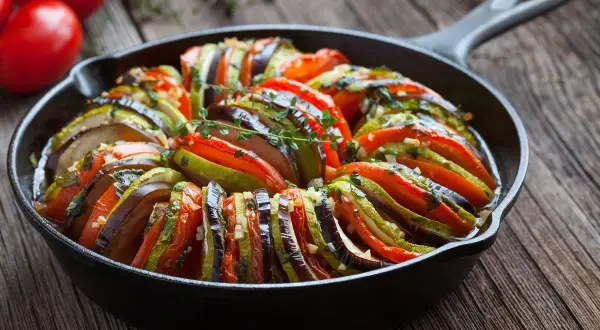 Ratatouille w żeliwnej patelni, klasyka kuchni francuskiej. Warzywa ułożone wachlarzowo, skropione ziołami.