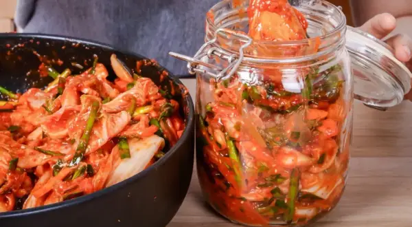 Przygotowanie kimchi: kapusta pekińska z sosem czosnkowo-paprykowym w misce i słoiku.