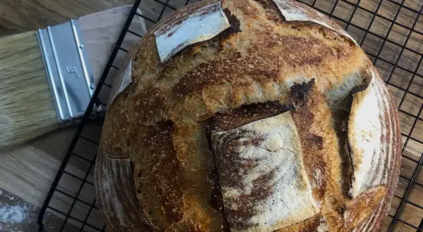 Złocisty, chrupiący chleb pszenny na zakwasie, gotowy do krojenia. Obok pędzel do pieczenia.
