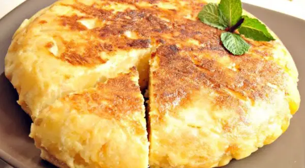 Pyszna tortilla de patatas, złocista i puszysta, z gałązką mięty na wierzchu.