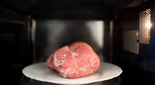 Zamrożony kawałek mięsa na talerzu w mikrofalówce. Szybkie rozmrażanie mięsa w kilka minut.