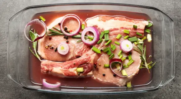 Peklowanie mięsa do pieczenia w szklanym naczyniu z cebulą, rozmarynem i pieprzem.