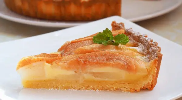 Kawałek pysznej, domowej tarta z gruszką, udekorowana listkiem mięty i posypana cukrem pudrem.