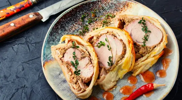 Pyszne ciasto francuskie na obiad, z soczystym mięsem i farszem, ozdobione gałązkami tymianku i papryczką chili.