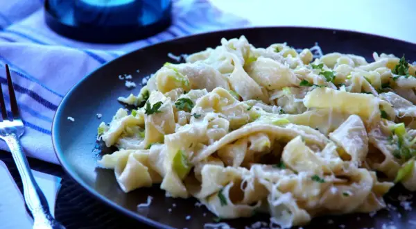 Pyszny makaron z porem, posypany parmezanem i świeżą natką pietruszki, czeka na widelcu.