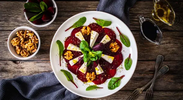 Eleganckie carpaccio z buraka z serem feta, orzechami włoskimi i świeżymi ziołami, podane na białym talerzu.