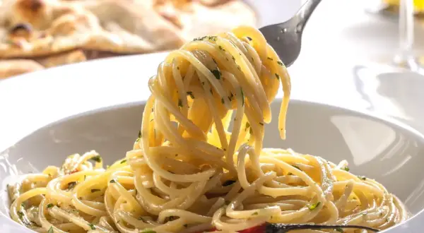 Pyszny, aromatyczny makaron spaghetti z czosnkiem i chili, idealny przepis na szybki makaron. Na talerzu widać też pieczywo.