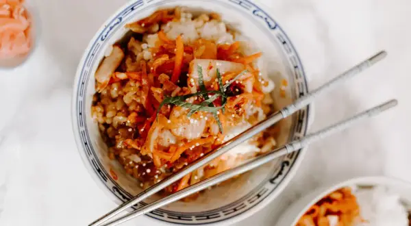 Miseczka ryżu z pikantnym kimchi i marchewką, pałeczki gotowe do jedzenia. Kimchi co to? To fermentowana kapusta.