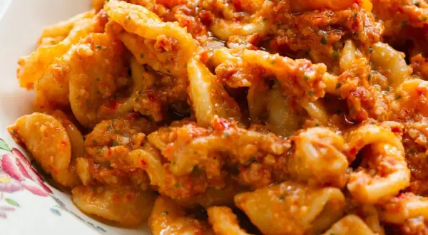 Pyszny makaron z pesto, pełen aromatycznych ziół i pomidorów, podany na talerzu z delikatnym wzorem.